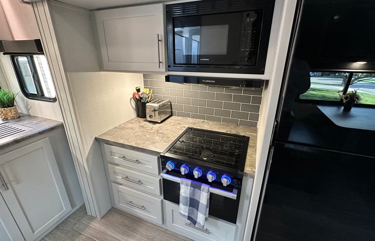 Microwave, 3-burner propane stove and oven - drawers stocked with utensils, pots and pans.