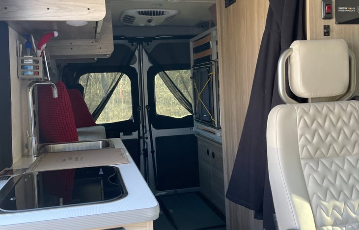 Rear view: Refrig, stove, & sink on left.  Two passenger seats, wet bath (toilet & shower), & queen-sized Murphy bed on the right. Additional storage area is all across the rear door space.
