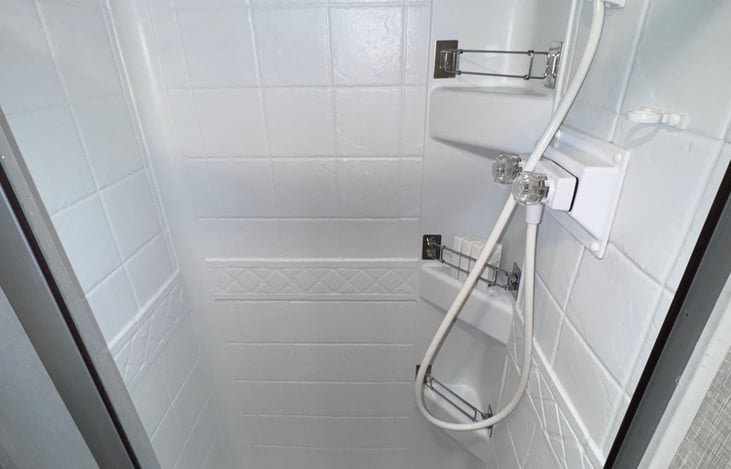 Private shower, with closing shower curtain on track, and multiple storage areas for toiletries.
