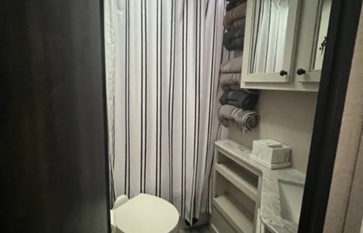 Bathroom with towel rack, medicine cabinets, shelves and small trash can. There is a hair dryer in the bathroom also.