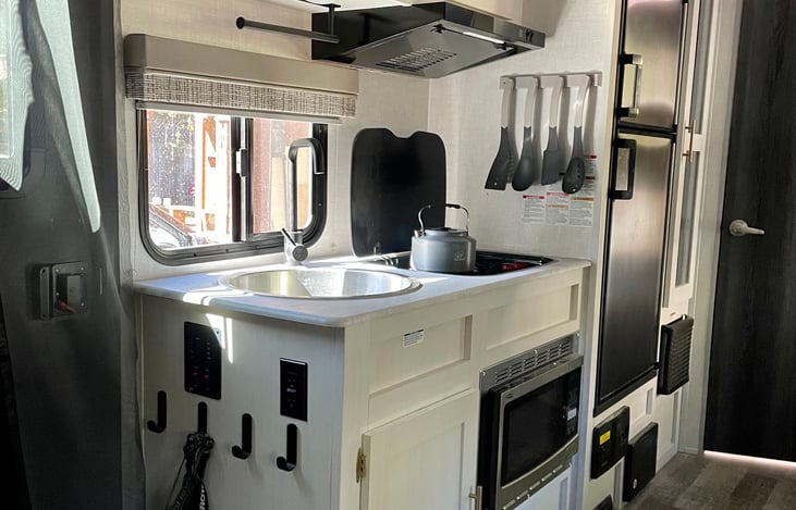 Kitchen stocked with pots, pans, tea kettle, utensils, cups, bowls, paper plates, seasonings, and more.