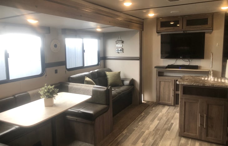 View from bunk beds.  Horseshoe dinette, jacknife couch that converts into double bed.  TV with overhead and below storage.  DVD player with AM/FM Bluetooth soundbar.  Kitchen sink to the right.