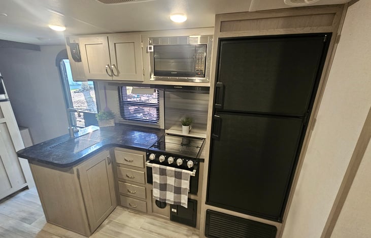 Kitchen offers a 3 burner stove top/oven combo. Range hood above the stove. Microwave. Stainless steel sink with a roll-up dry or rinse rack. Over head storage, storage under the sink and 4 drawers.