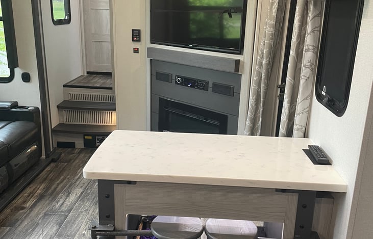 Looking out from kitchen area to TV and electric fireplace. Front door to the right and the couch to the left. Step lead up to the full bathroom and bedroom