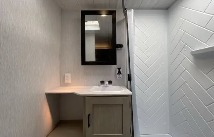 bathroom with working toilet, sink with hot and cold water valves as well as hot/cold shower heads. The mirror opens up to offer more bathroom storage.