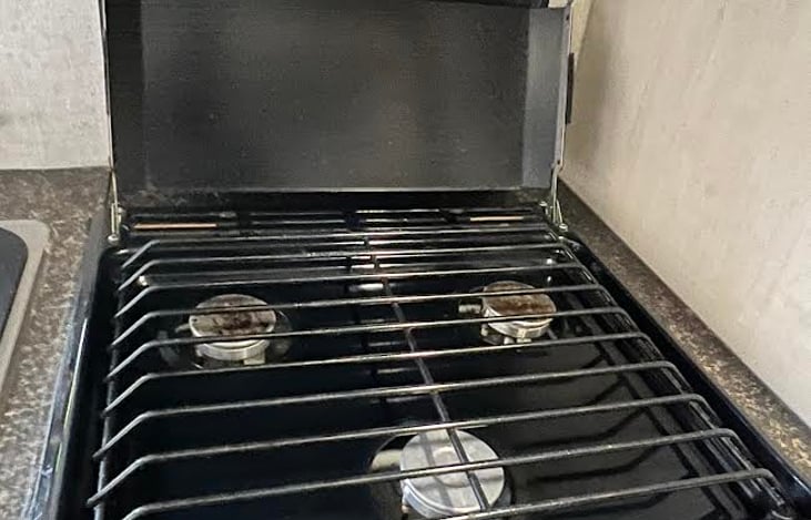 Very clean kitchen area has twin sinks, 3 burner stove and oven, overhead exhaust fan with light, 3 drawers, under and above sink storage area, and microwave oven.