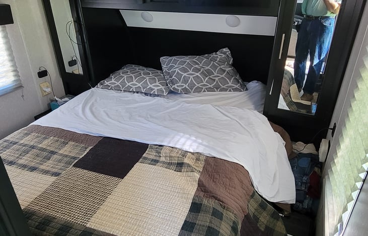 Bedroom has full-size queen mattress with storage underneath and a large closet to each side. Each side also has 2 USB ports and there's a 32" LCD TV mounted on the wall above a window.