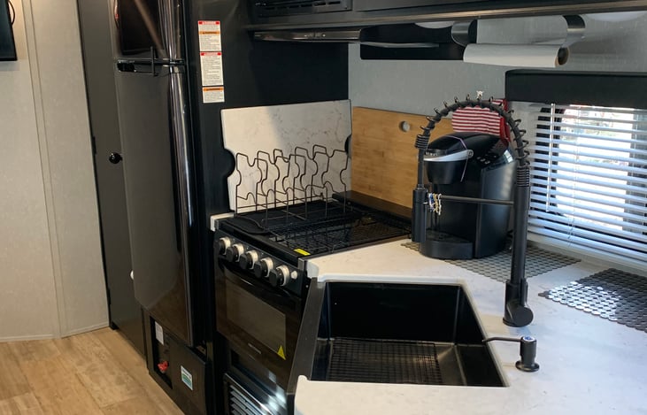 The kitchen features a full-size fridge, large pantry with plenty of room, glass top stove and range, wooden cutting board, and deep farmhouse style sink.