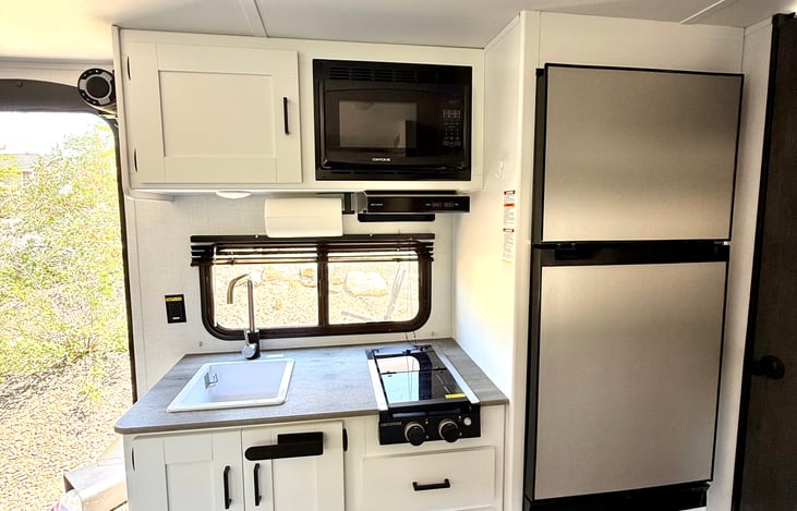 Large 7.7 cu. ft. fridge & freezer (works off of solar!!), two-burner stove, microwave, sink, and room for all your gear—kitchen ready for family meals on the road!