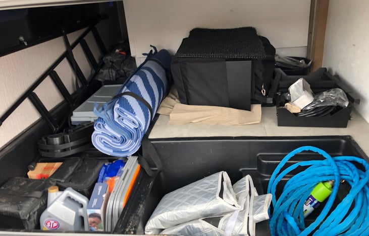 "Basement" and supplies with hoses, camp mat, Blackstone Grill, Window cover, buckets.