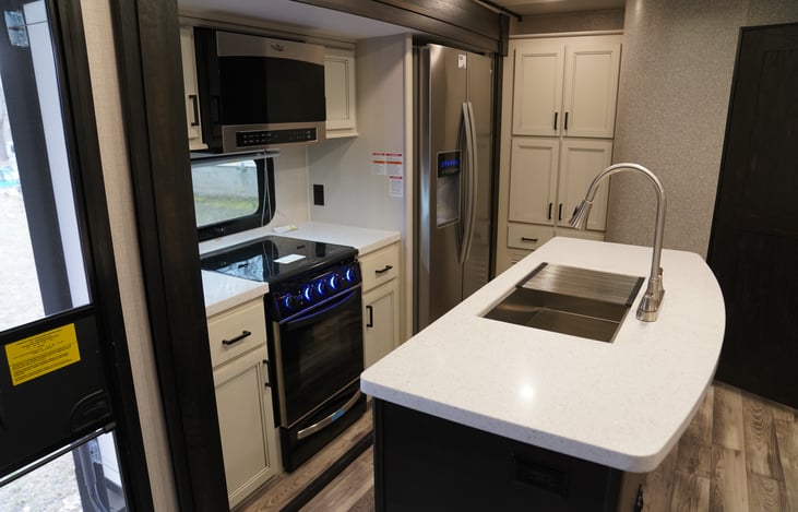 Large center island kitchen layout with residential fridge, oven, 3 burner stove, microwave, huge sink and plenty of pantry storage.