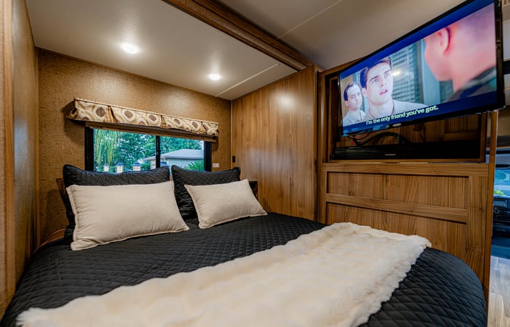 Queen bed shown with TV slide open and television swiveled to the bed.