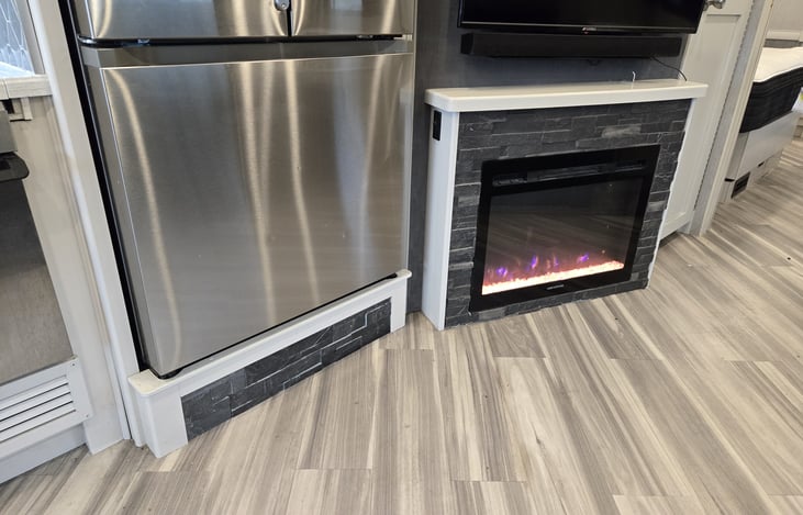 View of large residential electric refrigerator/freezer, electric fireplace (with heater when desired) and above LED TV.
