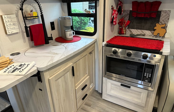 Convection microwave, glass covered 3 burner cooktop, circular sink with countertop cover, pull down faucet, wireless integrated phone charger, and flip up counter extension. Kitchen items included