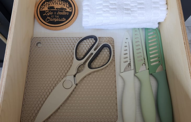 Kitchen drawer with essentials. (Knives, hand towel, coasters, silicone pot holders, and scissors.)