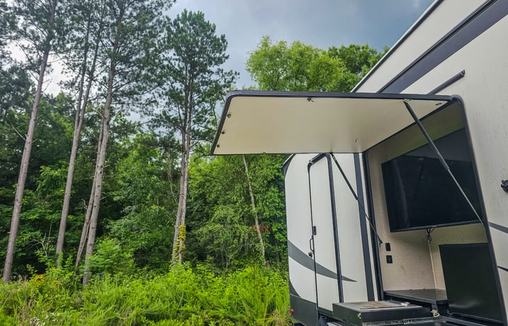 Outdoor kitchen with gas grill, mini fridge and TV.