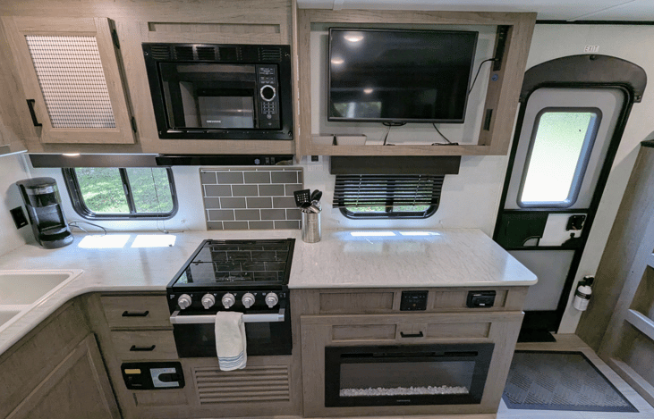 Spacious and cozy interior with well-equipped kitchen, large refrigerator, ample counter space, electric fireplace, TV, stereo, and bunks.