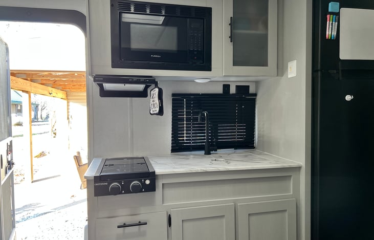 Kitchen with two propane burners with glass cover and range hood with light and exhaust, large farm house sink with recessed cover and microwave