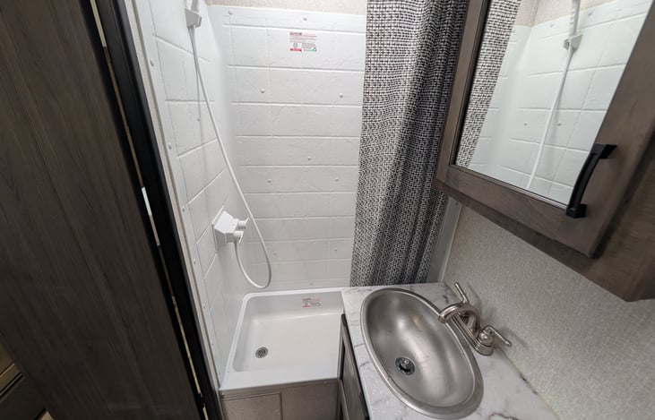 Full bathroom featuring a spacious walk-in shower with a overhead skylight for extra headroom, porcelain foot-flush toilet, vanity sink, and mirror with medicine cabinet storage.