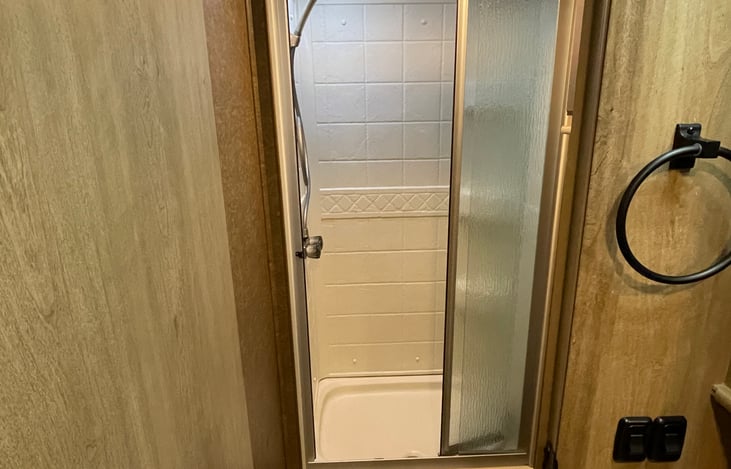 Full size shower with a glass door in the bathroom with a ceramic toilet.