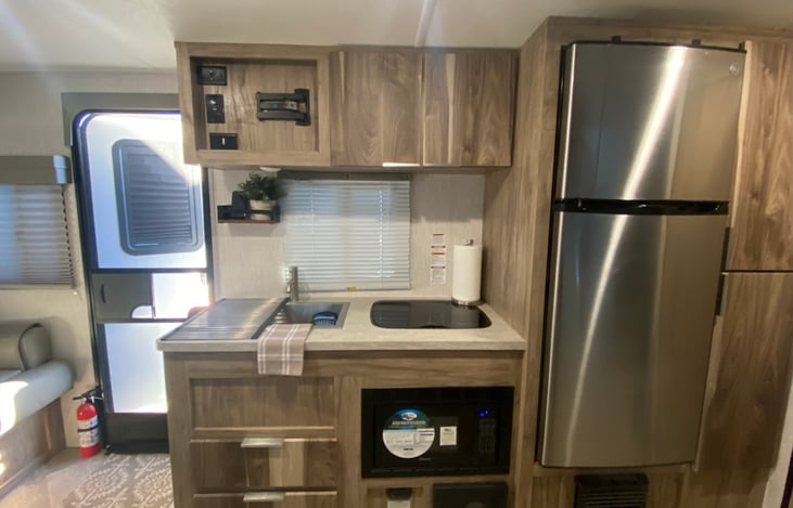 Kitchen area with single basin stainless steel sink, cook top, two drawers, microwave, and refrigerator.