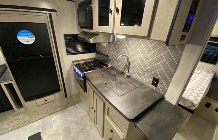 Kitchen area with range, overhead microwave, refrigerator, and cabinetry