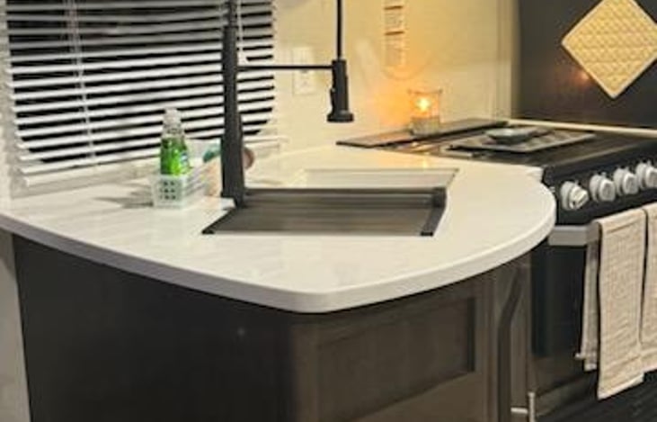 Kitchen sink, oven and stovetop, full fridge and window in kitchen/cooking area.