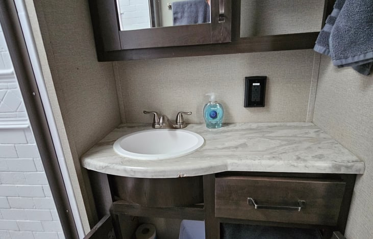 Bathroom cupboard doors open to show TP holder and extra towels.