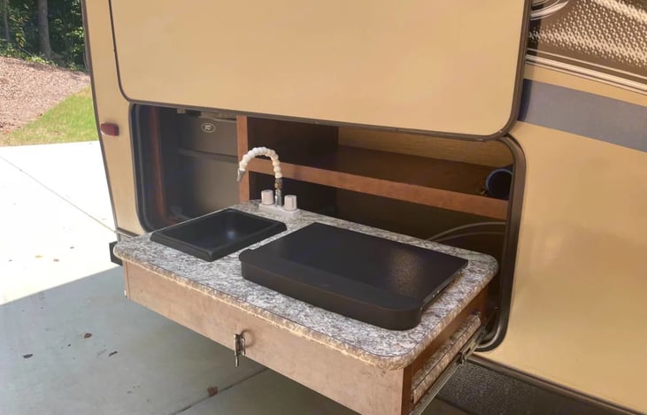 Outdoor kitchen with 2 burner stove, sink, and mini fridge.