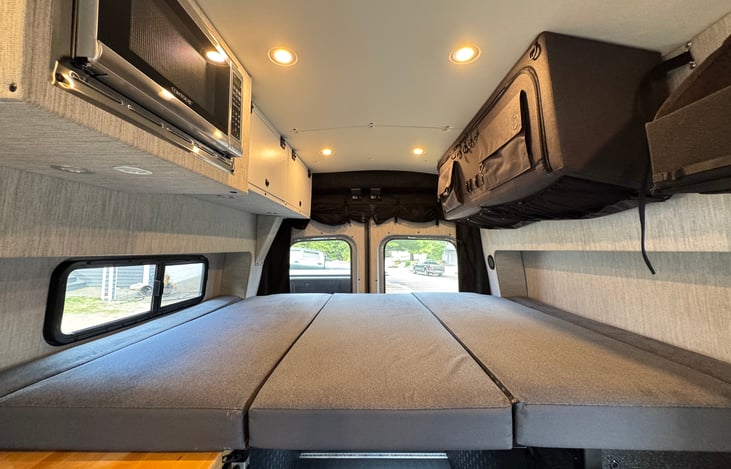 The pull-down Murphy bed offers a comfy sleep space and folds flat to save room. Above it, built-in overhead storage keeps clothes, gear, and essentials organized and easily accessible.