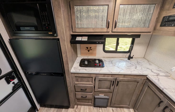 Spacious rear kitchen layout with ample counter space, double-door fridge, stove, microwave & deep sink. Perfect for prepping campsite meals with all the comforts of home!