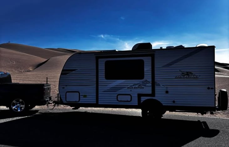 A sleek travel trailer hitched and ready for adventure, set against stunning desert dunes for the perfect getaway vibe.