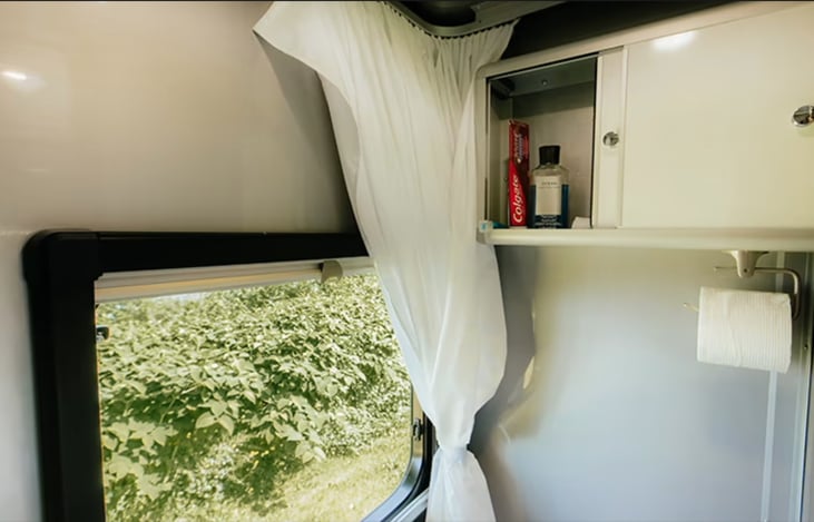 Bathroom with large window and storage above toilet. Shower curtain goes 360 degrees around bathroom for taking a shower.