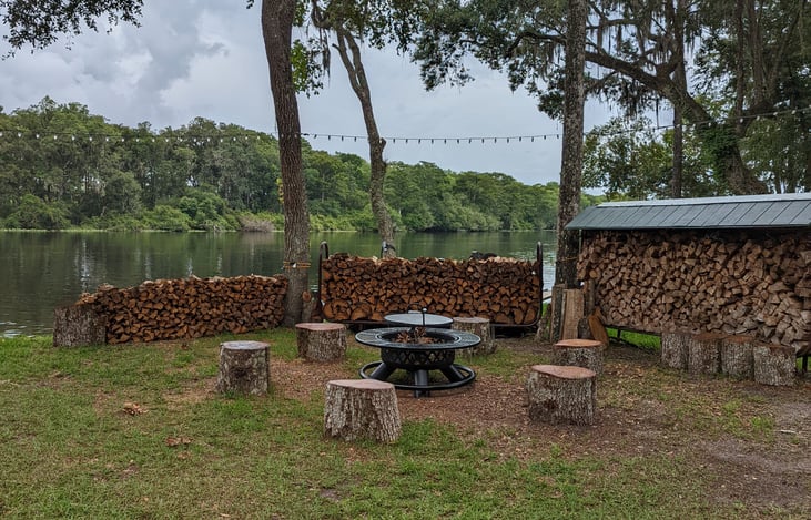 View of fire pit with Suwannee River in background. No need to bring firewood. You can  use the logs as seats or end tables. Chairs are provided.