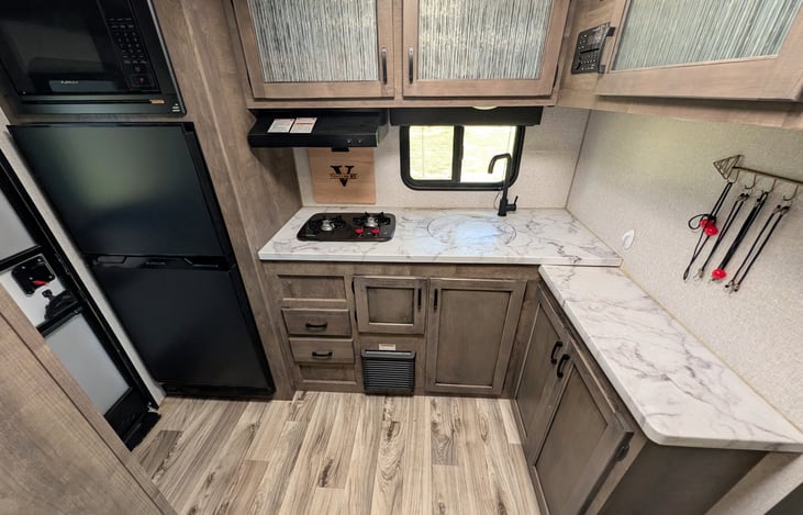 Spacious rear kitchen layout with ample counter space, double-door fridge, stove, microwave & deep sink. Perfect for prepping campsite meals with all the comforts of home!