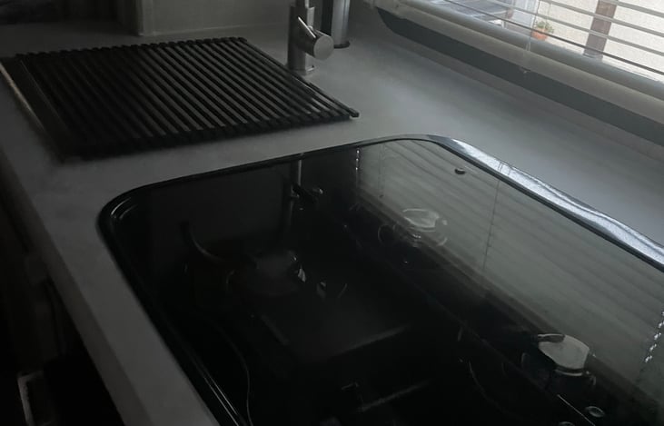 Four burner stove with cover, stainless steel sink and faucet with dish rack cover, kitchen window with blinds, all new.