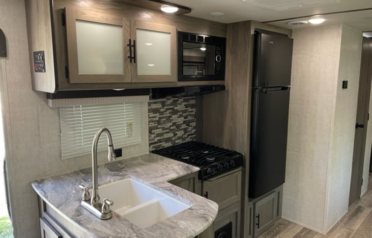 Kitchen with 3 burner cooktop, refrigerator, microwave and residential style sink with high rise faucet and sprayer.