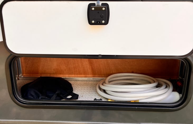 Fresh water hose, 30-amp shore power connection cable and power adapters cubby.