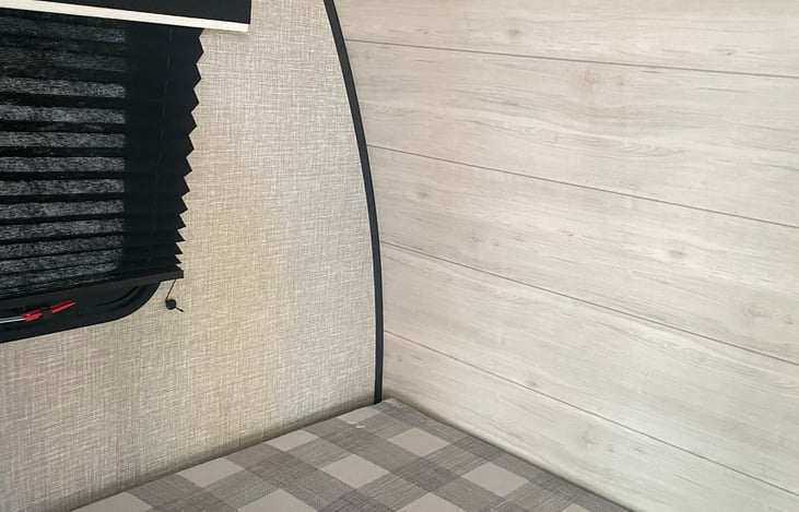 Left side of queen size bed, window with shutters, and vinyl wall.