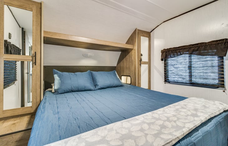 Master bedroom with full size queen bed with comforter, blanket and 4 pillows. Each side has its own hanging area for clothes and charging ports for phone.