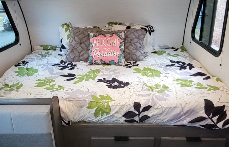 A queen bed with a shelf above with bins for storage and four drawers built into the base.