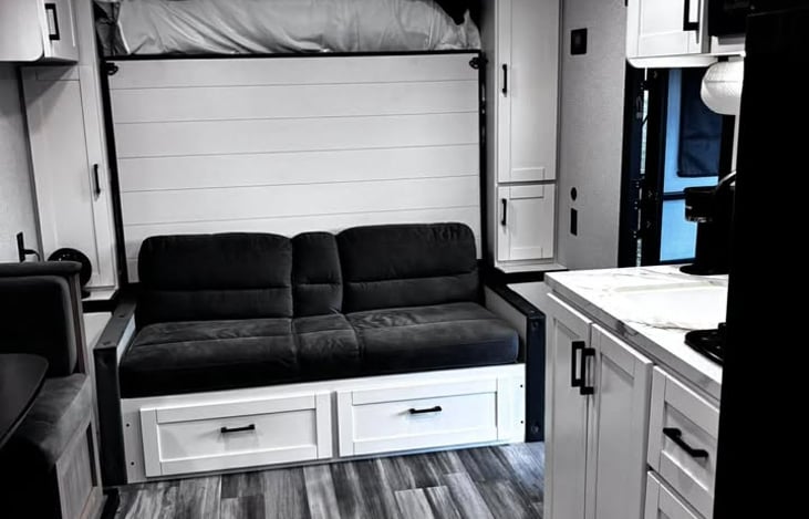 A bright, modern RV living space featuring a comfy sofa, fold‑down bed, and a clean, well‑equipped kitchenette designed for effortless travel comfort.