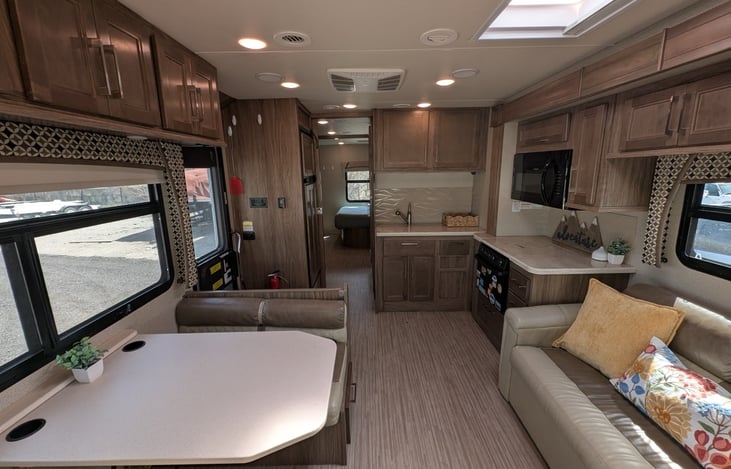 Spacious living area features comfortable sofa, dinette, and fully equipped kitchen. Natural light streams through the skylight and windows. Modern amenities include microwave, large refrigerator, and