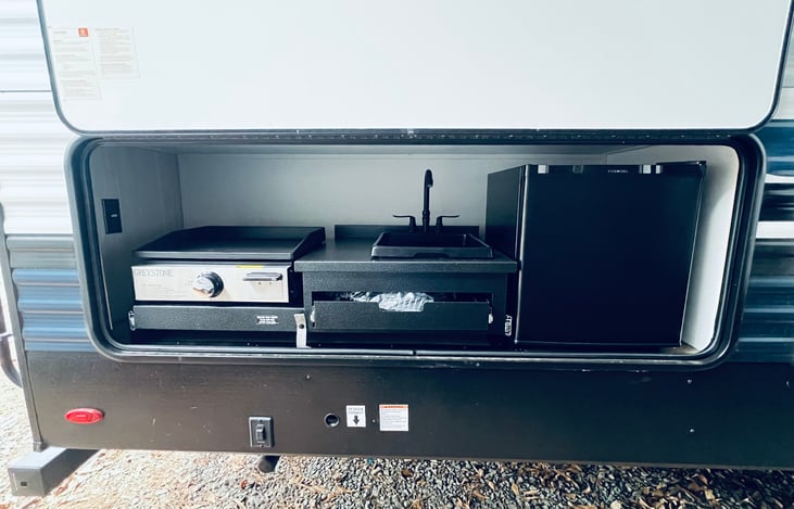 Outdoor kitchen area with a small fridge, cooktop griddle and sink