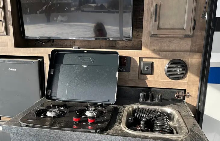 Outdoor kitchen with sink, stove top, mini fridge, and large tv.