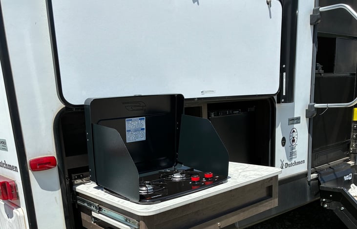 This outdoor kitchen has a two-burner gas stove, a refrigerator, and a pull-out countertop extension. Enjoy cooking and entertaining outside with these convenient features.