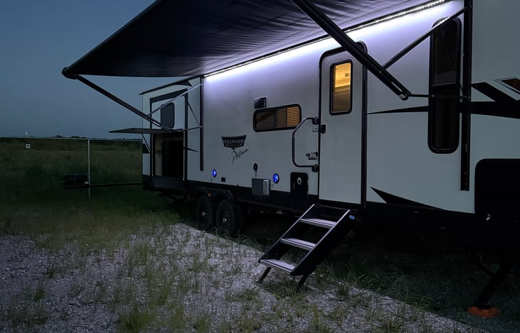 Outdoor space with awning, LED lights and Bluetooth speakers. Outdoor kitchen with mini fridge, sink and grill.