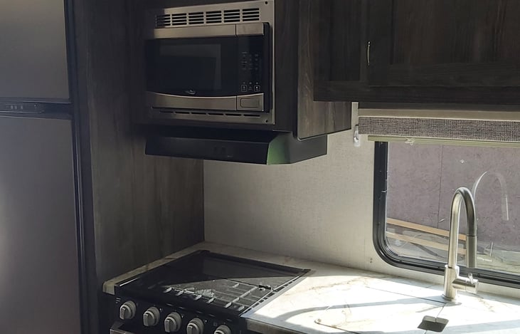 Farm-style kitchen with microwave, lights, fans, gas top stove and oven.