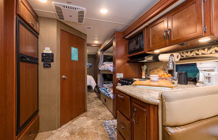Refrigerator to the left. Entrance to the bathroom in the center. Double bunk beds in the back.