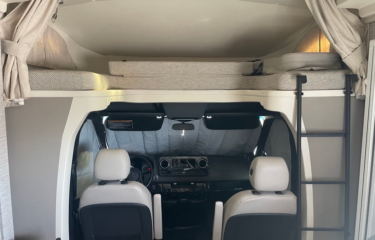 Above cab bed or storage with ladder access and curtains for privacy.